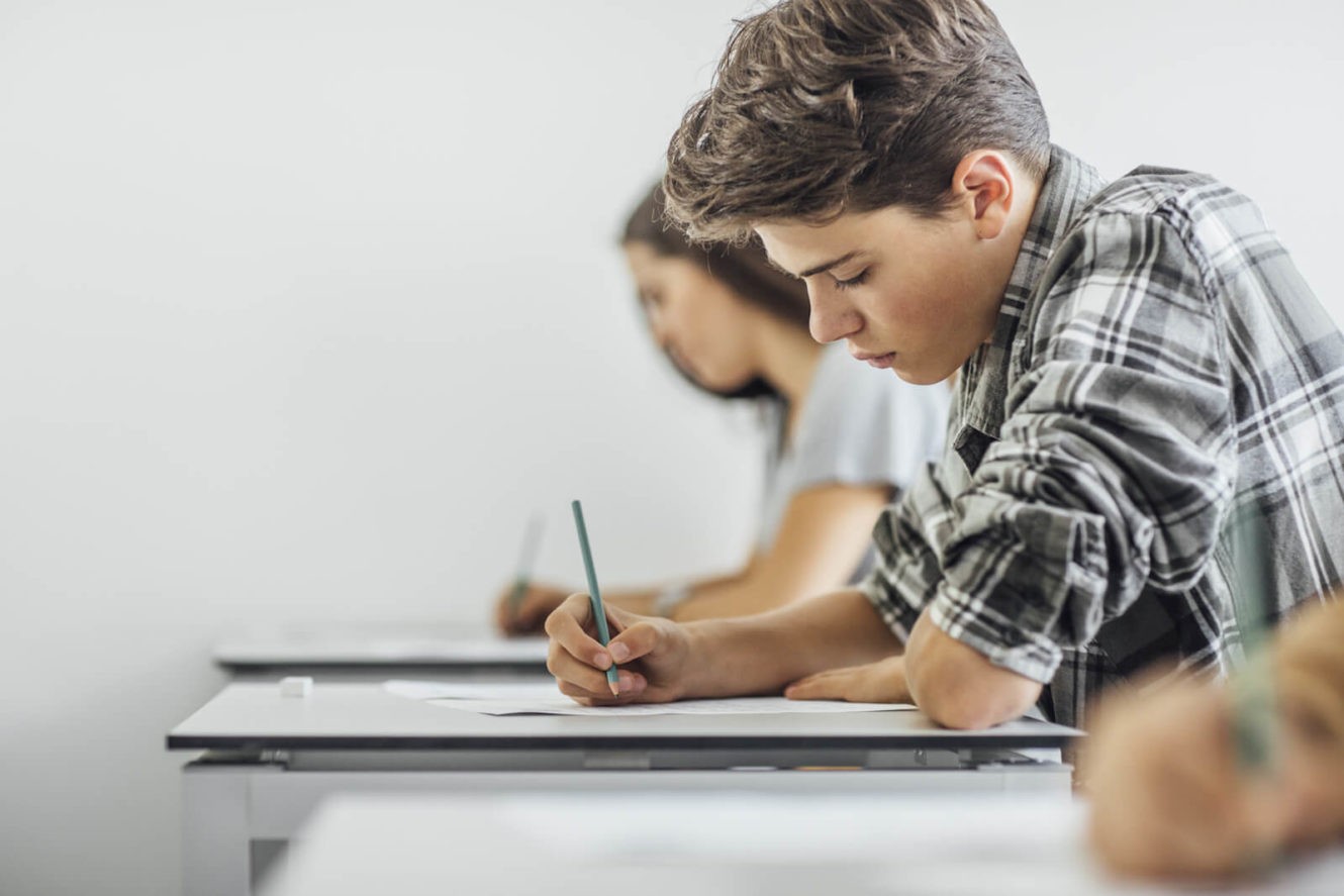 Boy writing on piece of paper at his desk