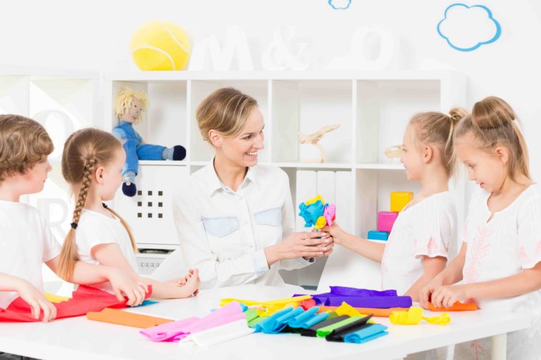 Female teacher and young students working on crafts at a table