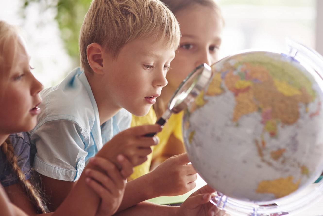 Young kids holding a magnifying glass and looking at a globe