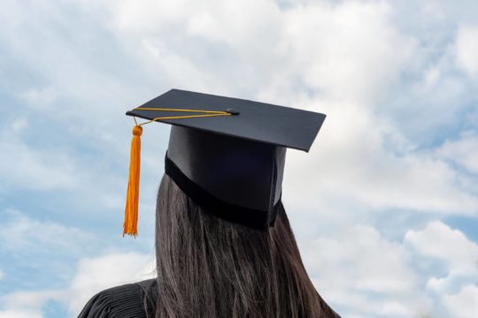 High school graduate wearing a cap and gown with a sky background.