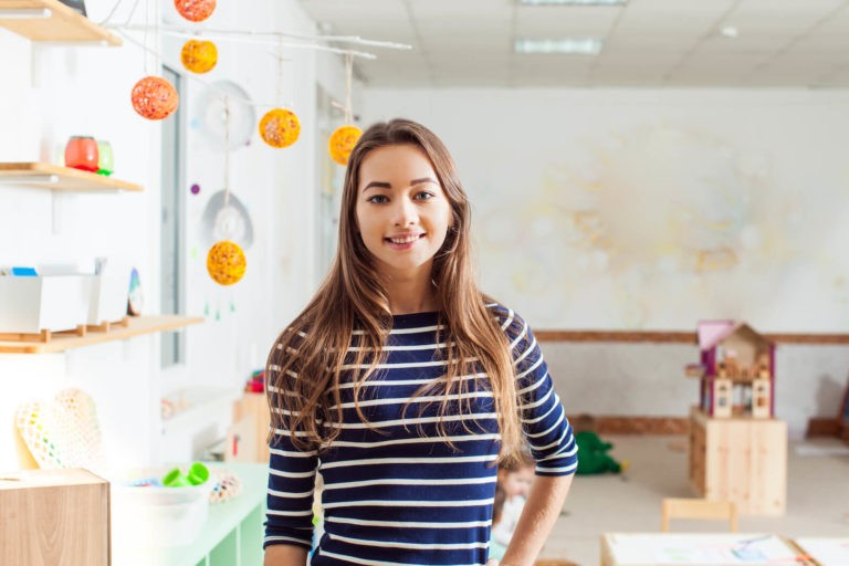 Young teacher standing and smiling at the front of her classroom.