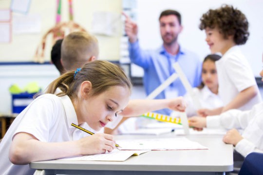 Young student working independently with classmates and her teacher in the background.