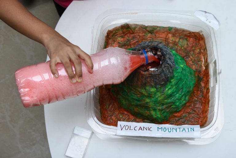 Student pouring solution into a homemade volcano mountain.