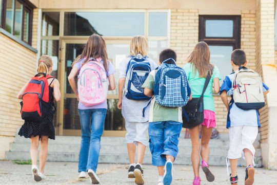 Group of students wearing backpacks approaching the school doors.