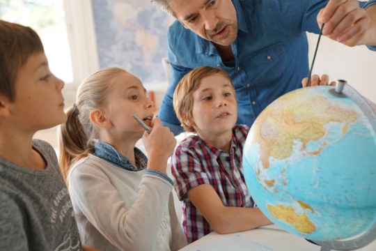 Teacher pointing to something on a globe with students gathered around.