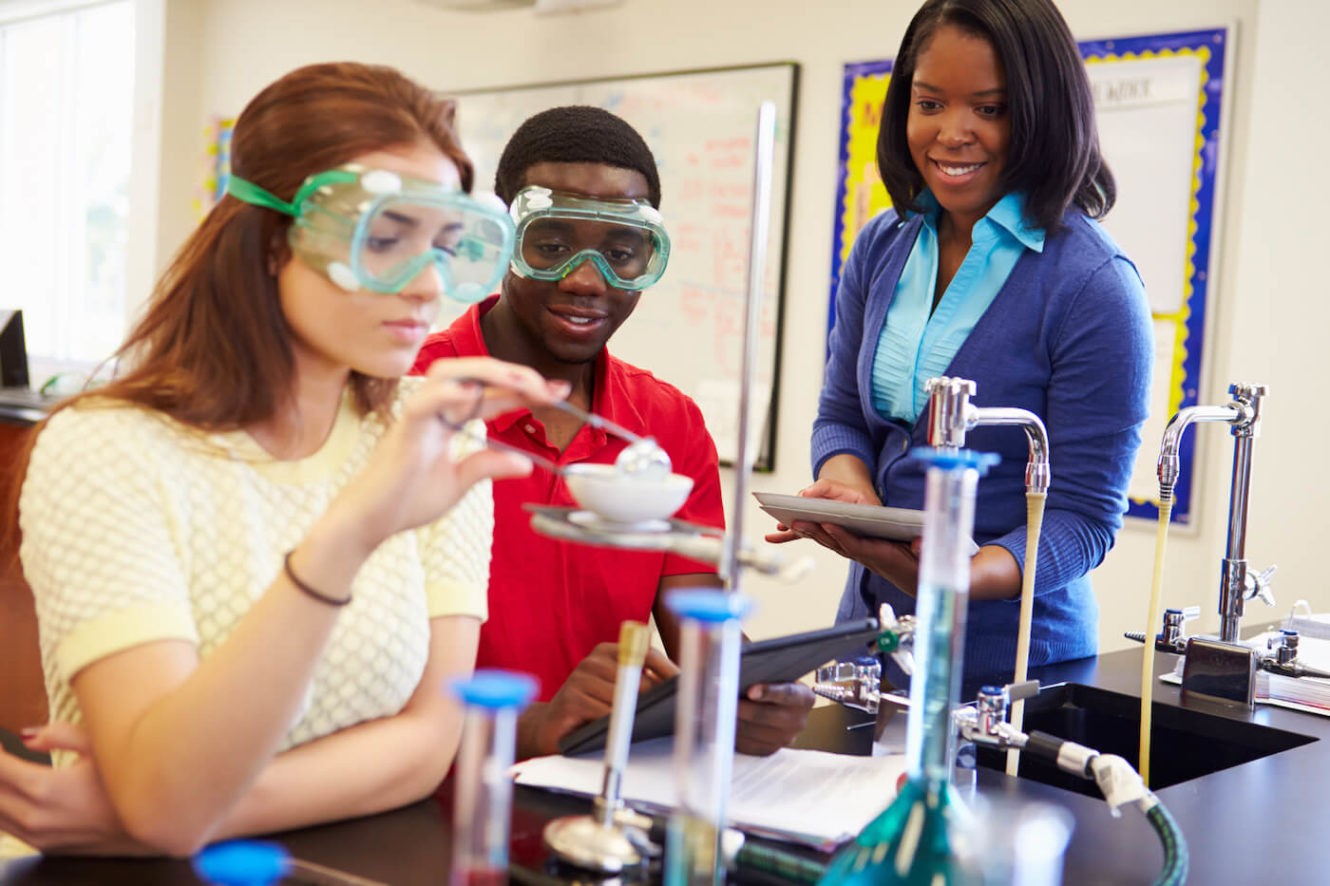 Two high school students working on science lab project while being supervised by a female teacher