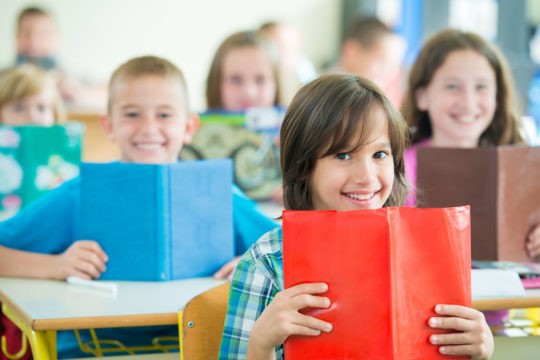 A group of young students smiling while holding their books up