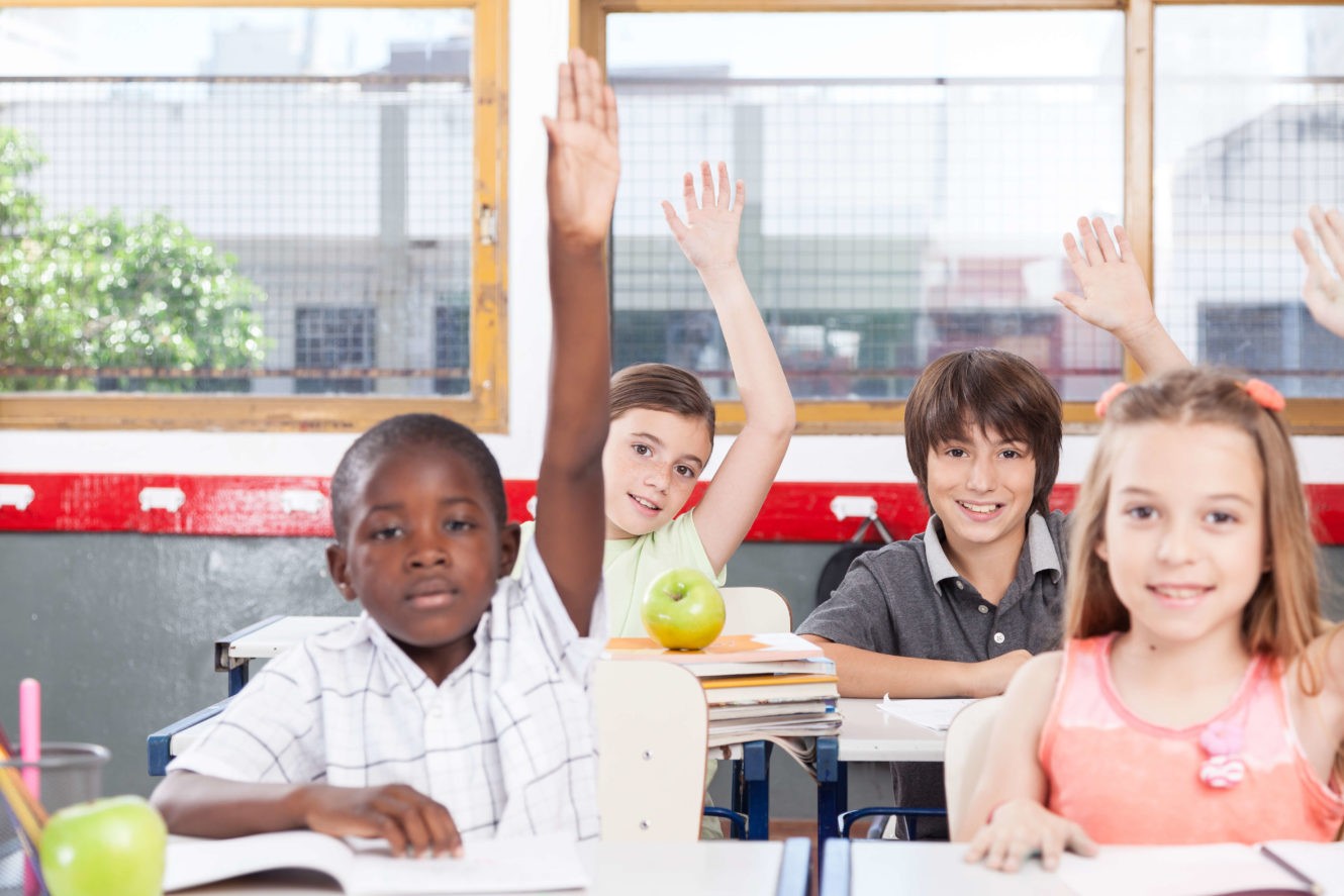 Students sitting at desks while raising their hands