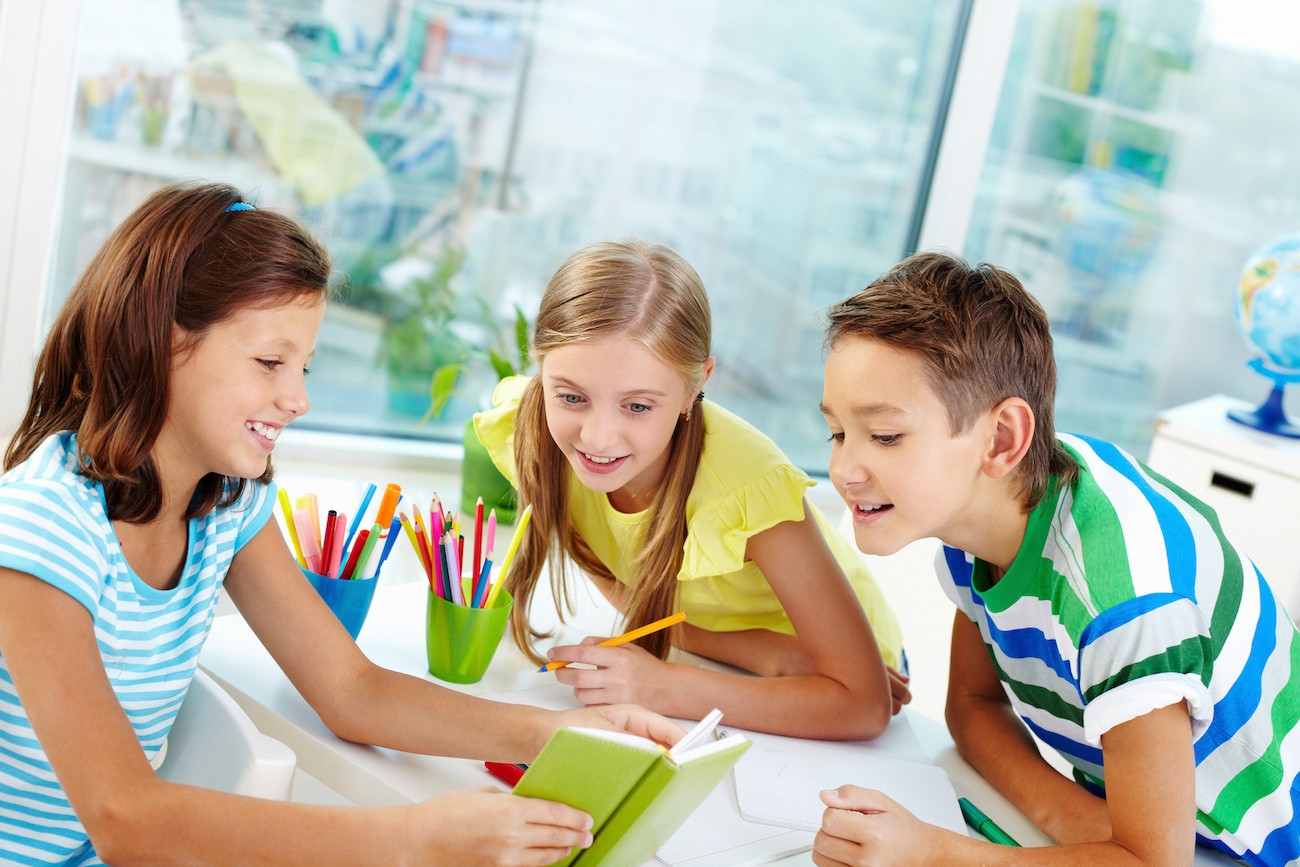 Young smiling students hovering over a book they are reading together