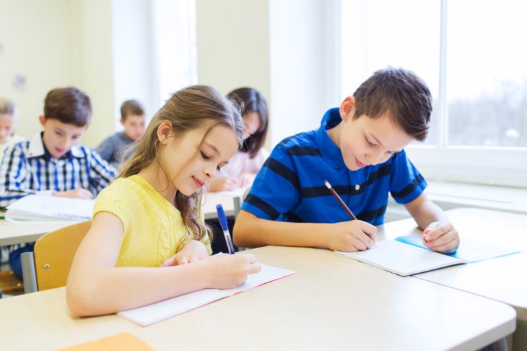 Two young students sitting at desks writing in notebooks.