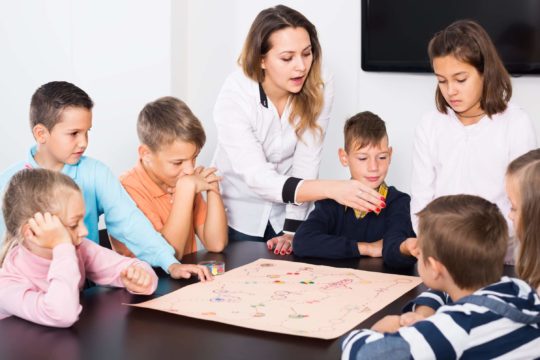 Group of young students playing a game together at a table with a teacher giving instruction.
