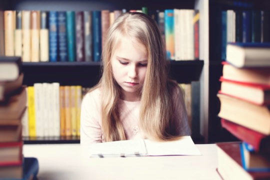 Young girl sitting a table in library reading notebook