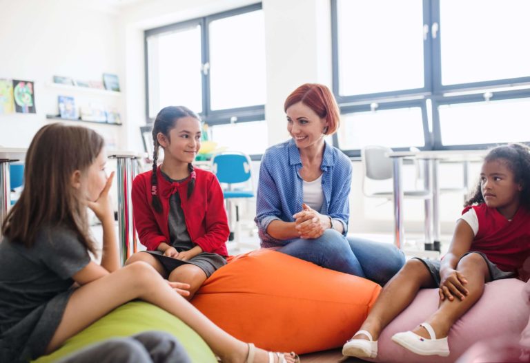 Young students and teacher sitting on beanbags in a classroom.