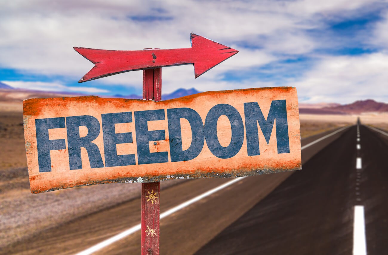 Road sign with the word ‘Freedom’ and road in the background