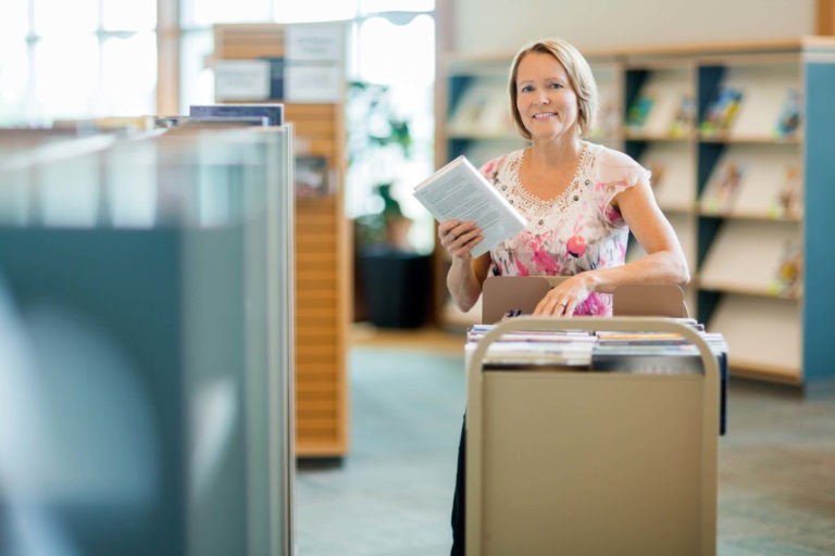 Smiling librarian walking around with cart of books.