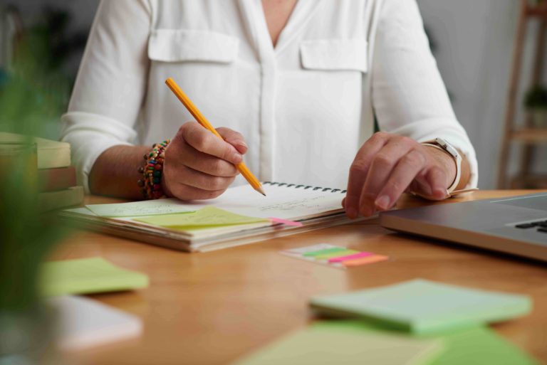 teacher sitting at her desk making notes in a planner with sticky notes.