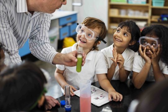 Teacher helping a group of youg students with a science experiment