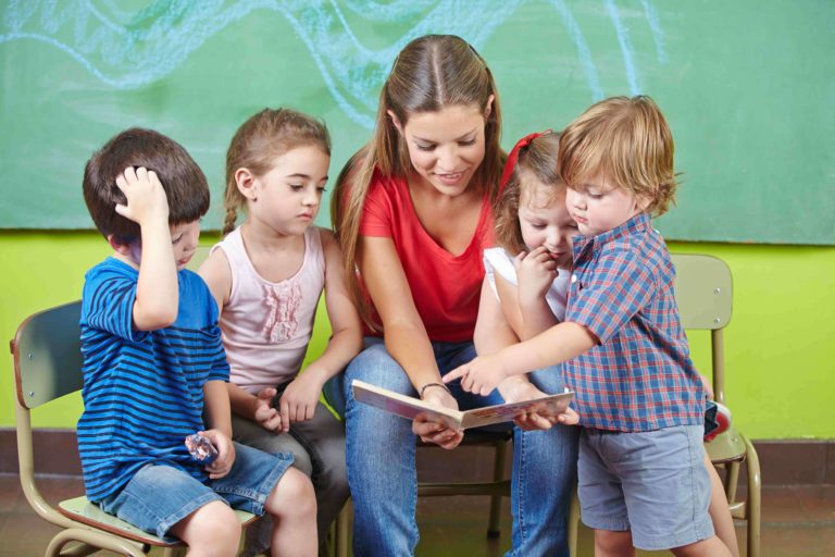 Young children standing around their teacher reading a book