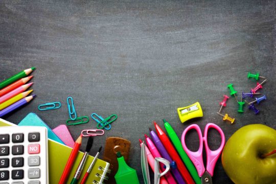 Various school supplies in front of a chalkboard background