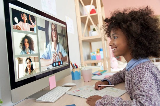 Young girl sitting at her desk in a Zoom class with classmates.