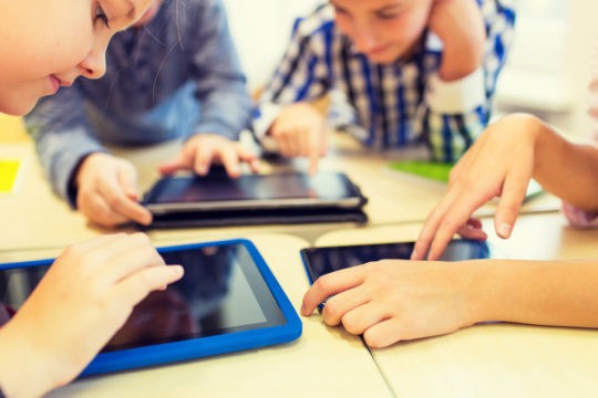 Group of students sitting at desks and using tablets.