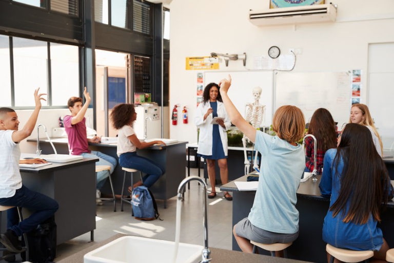 High school students with their hands raised in a science classroom.