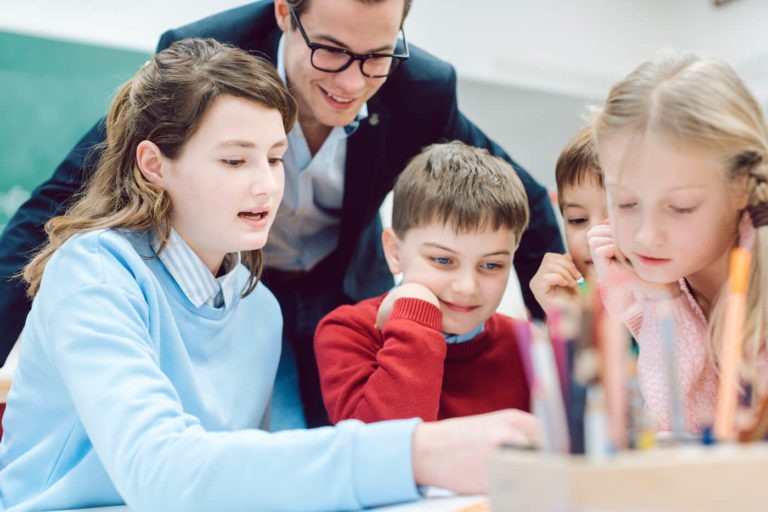 Group of young students sitting around a table with their teacher.