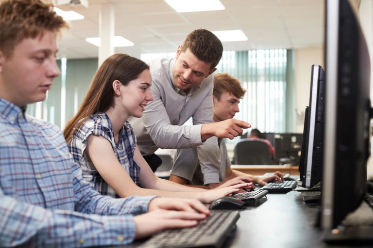 Teacher pointing out something to a high school student on a computer.