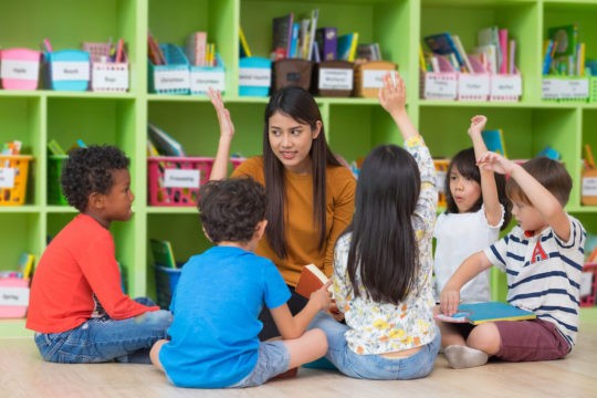 Teacher reading to a group of young students sitting on the floor in a classroom.