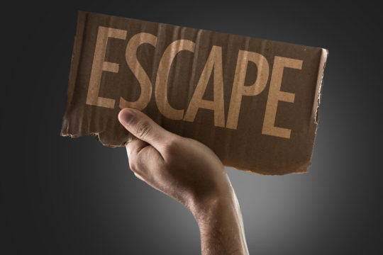 Hand holding up a cardboard sign reading ‘escape.’