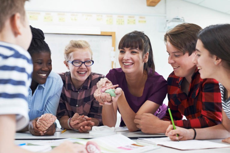 Teacher showing middle school students something while sitting around a table.