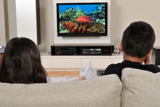 Two kids sitting on a couch watching TV.