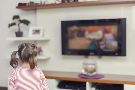 Young girl sitting on a couch watching TV.