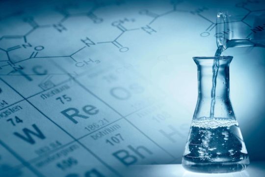 Liquid being poured into a flask with periodic table in the background