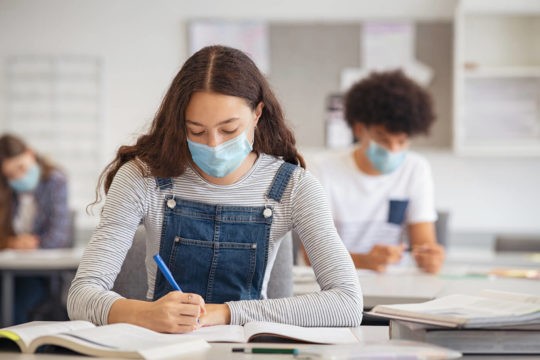 High school students in class wearing masks and writing in notebooks.