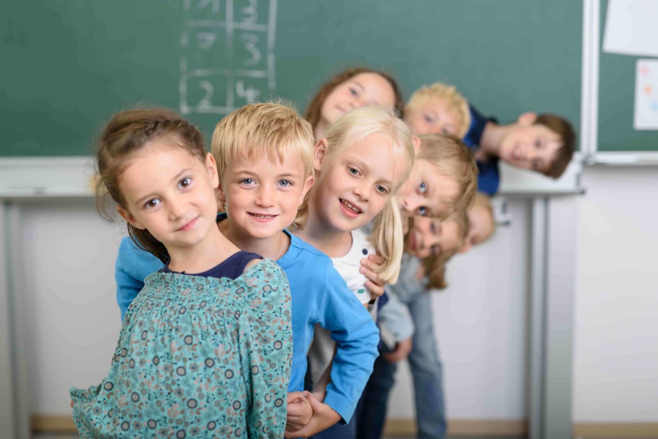 A line of smiling students in front of a chalkboard with numbers