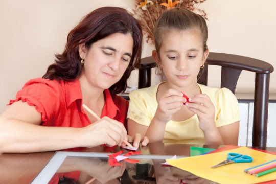 Mother and young daughter working on an art project at a table.