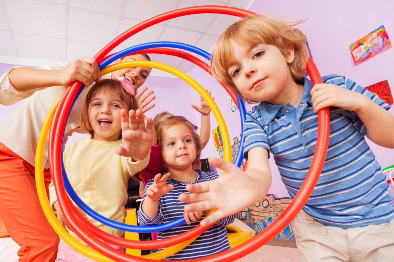 Young smiling students holding hula hoops with their teacher