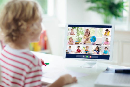 Young boy at a table during a Zoom class with his teacher and classmates.