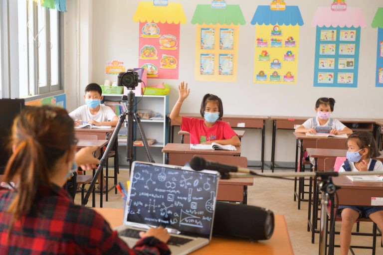 Teacher at her desk teaching in-person and online students at the same time.