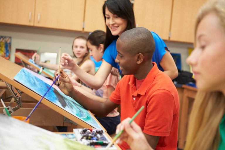 High school students painting in art class with a teacher observing.