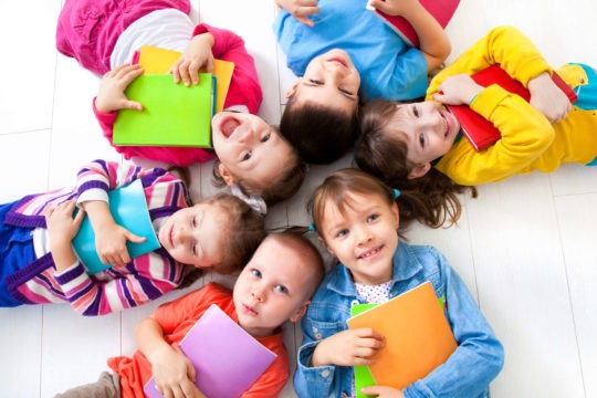 A group of smiling children laying on the ground in a circle holding books