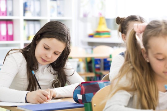 Young girl writing on paper in class