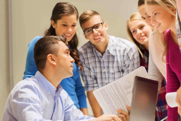 Male teacher and group of smiling students looking at a paper