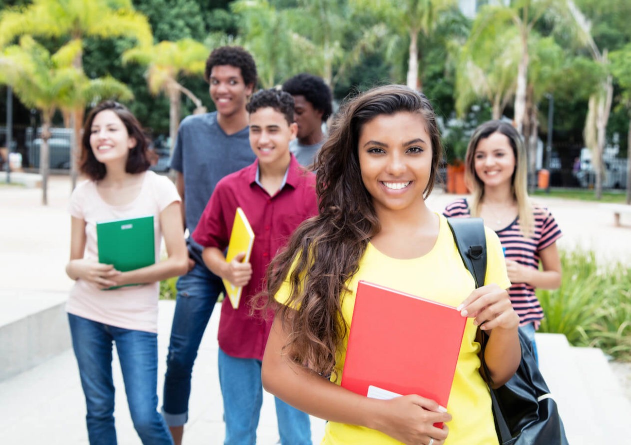 A group of multiracial high school students holding books and smiling
