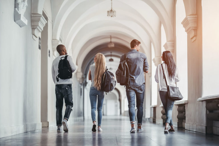 Four students walk in a university hall, talking to each other.