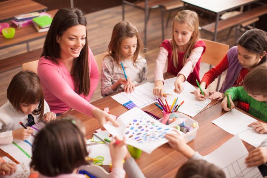 Young student sitting around a table with their teacher drawing.