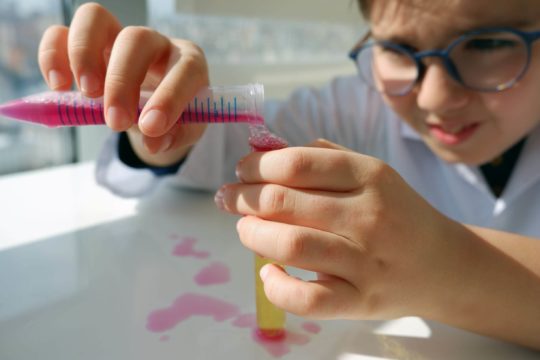 Young boy wearing glasses pouring liquid from one test tube into another.