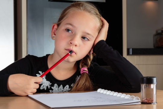 Young girl holding pencil to her mouth while thinking