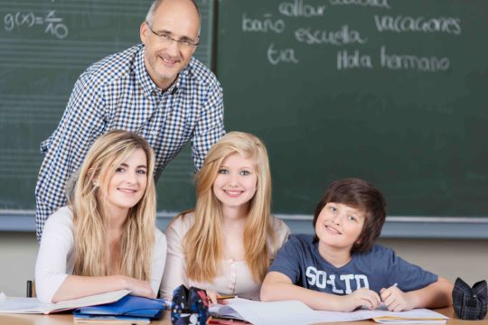 Male teacher standing in front of a chalkboard behind a group of students